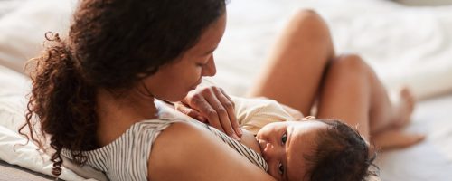 High angle portrait of young African-American mother breastfeeding cute baby boy with child looking at camera, copy space